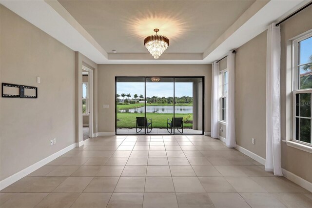 tiled empty room featuring an inviting chandelier, a raised ceiling, a water view, and a healthy amount of sunlight