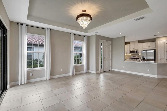 unfurnished living room featuring an inviting chandelier, a tray ceiling, and plenty of natural light