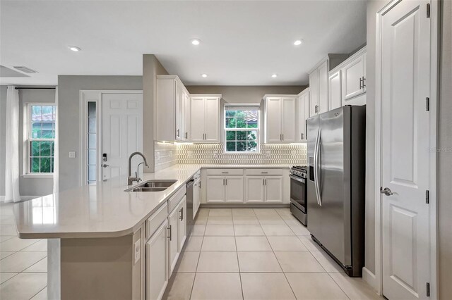 kitchen featuring decorative backsplash, light tile patterned flooring, white cabinets, stainless steel appliances, and sink