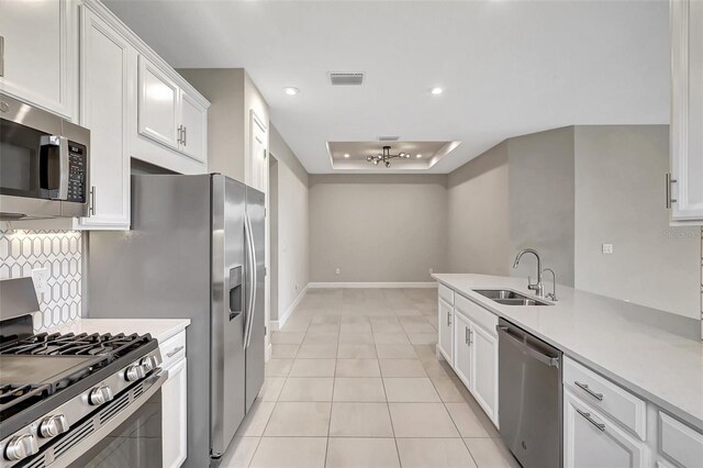 kitchen featuring a tray ceiling, light tile patterned flooring, sink, white cabinets, and appliances with stainless steel finishes