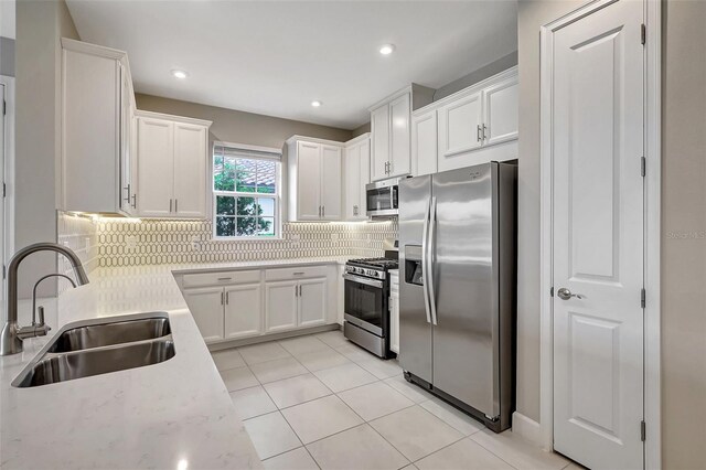 kitchen featuring sink, white cabinets, backsplash, appliances with stainless steel finishes, and light tile patterned floors