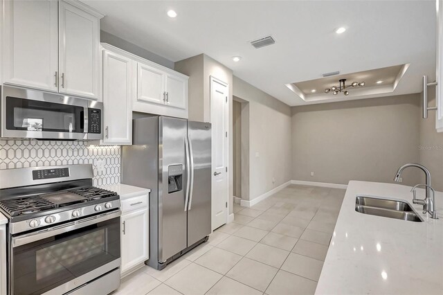 kitchen featuring white cabinets, stainless steel appliances, sink, and a tray ceiling