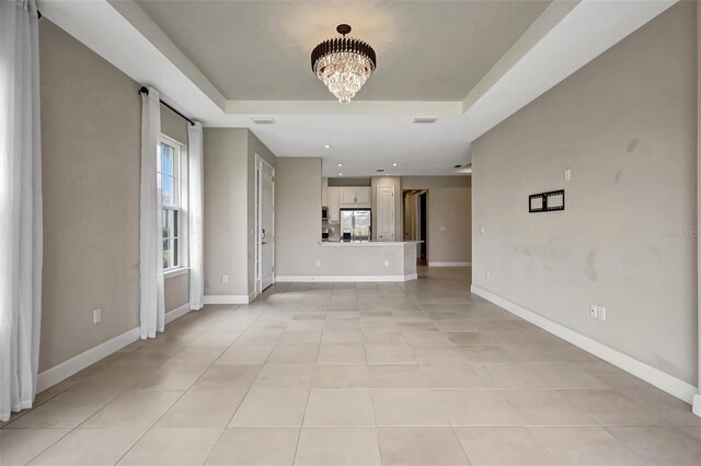 unfurnished living room with a chandelier, a tray ceiling, and light tile patterned floors