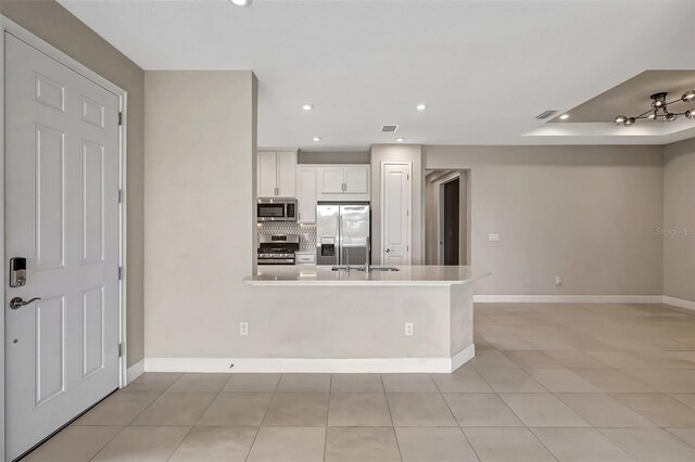 kitchen with appliances with stainless steel finishes, white cabinetry, backsplash, kitchen peninsula, and light tile patterned floors