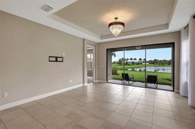 unfurnished room featuring a notable chandelier, a wealth of natural light, a water view, and a tray ceiling