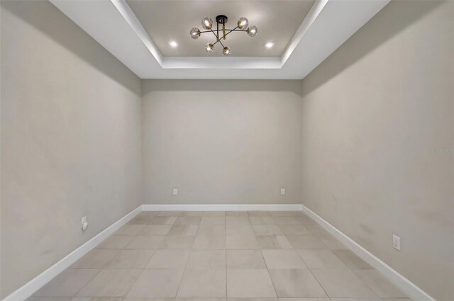 empty room featuring an inviting chandelier, a tray ceiling, and light tile patterned floors