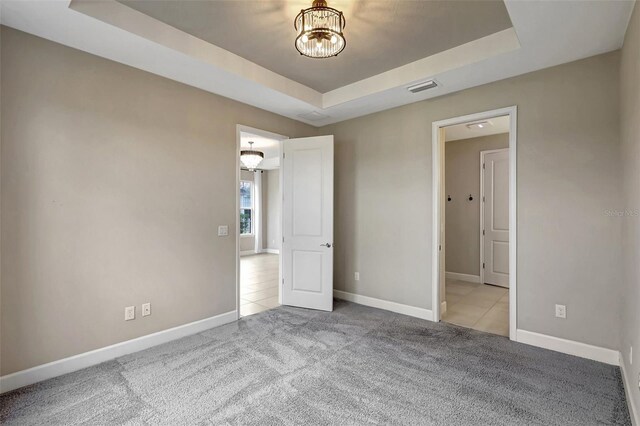 unfurnished bedroom featuring an inviting chandelier, light colored carpet, and a raised ceiling