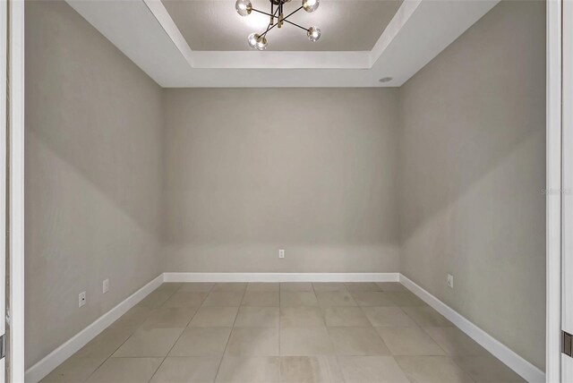 tiled spare room with a notable chandelier and a raised ceiling