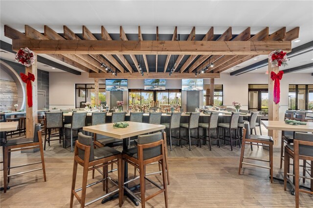 dining space featuring track lighting, beamed ceiling, bar, and light hardwood / wood-style floors