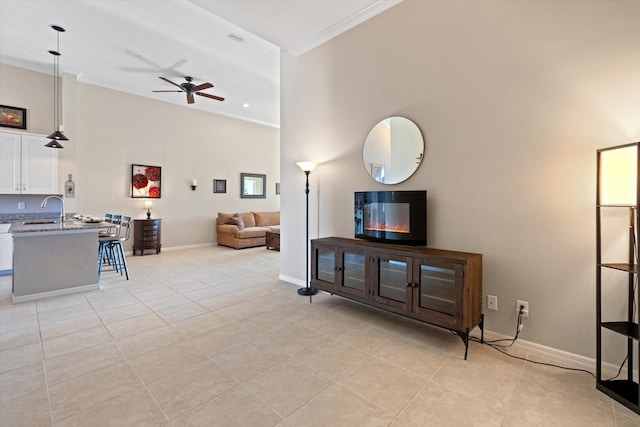 living area with light tile patterned floors, baseboards, ceiling fan, a high ceiling, and crown molding