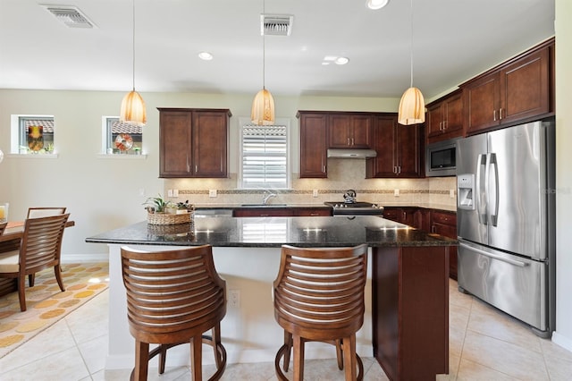 kitchen with a center island, appliances with stainless steel finishes, dark stone countertops, and hanging light fixtures