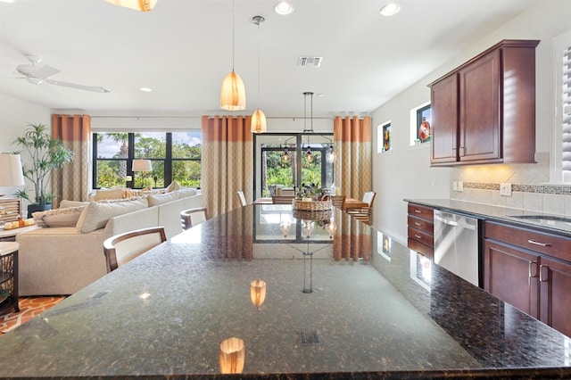 kitchen with decorative light fixtures, dishwasher, a center island, ceiling fan, and dark stone counters