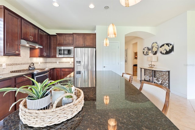 kitchen featuring dark stone countertops, light tile patterned floors, stainless steel appliances, pendant lighting, and decorative backsplash