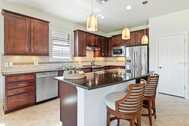 kitchen featuring dark stone countertops, stainless steel appliances, decorative light fixtures, a kitchen island, and a breakfast bar area