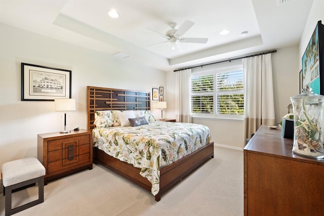 bedroom featuring a tray ceiling, light carpet, and ceiling fan