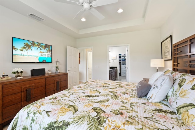 bedroom with ceiling fan, a raised ceiling, and ensuite bathroom