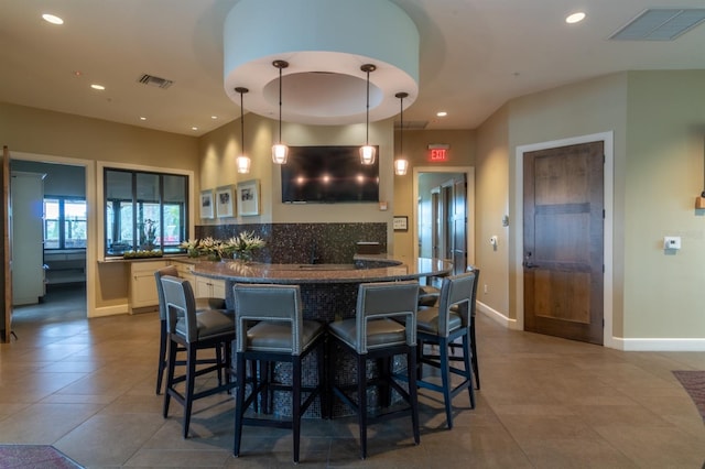 kitchen with tile patterned floors, pendant lighting, decorative backsplash, and a breakfast bar