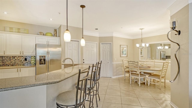 kitchen featuring stainless steel fridge, an inviting chandelier, white cabinets, and pendant lighting