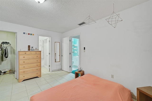 bedroom featuring connected bathroom, light tile patterned floors, a textured ceiling, a walk in closet, and a closet