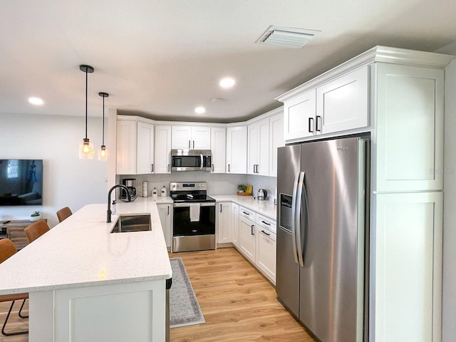 kitchen featuring a kitchen breakfast bar, appliances with stainless steel finishes, light hardwood / wood-style floors, kitchen peninsula, and sink