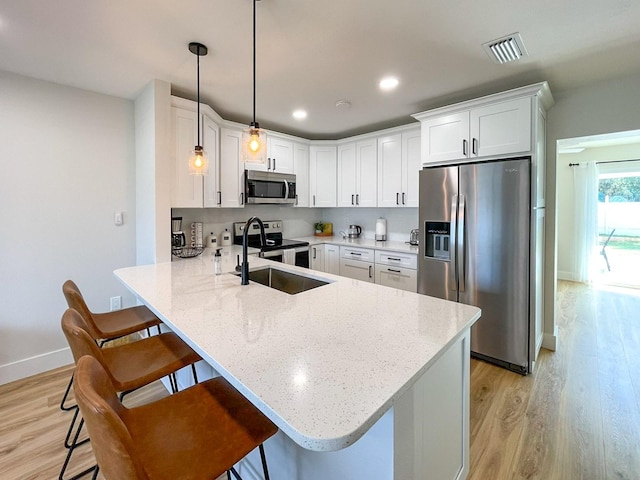 kitchen with light hardwood / wood-style flooring, decorative light fixtures, sink, a breakfast bar, and appliances with stainless steel finishes