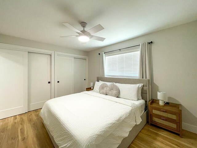 bedroom featuring ceiling fan, light wood-type flooring, and multiple closets