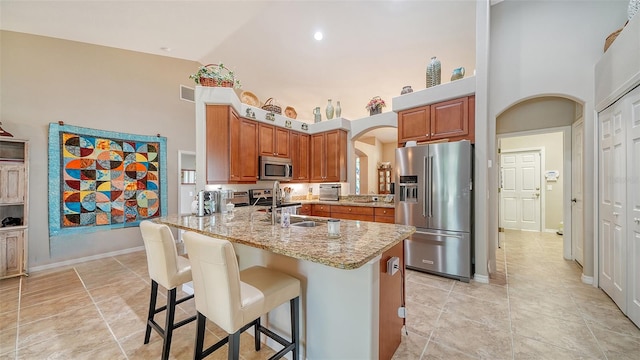 kitchen featuring light stone counters, stainless steel appliances, kitchen peninsula, a kitchen bar, and a towering ceiling