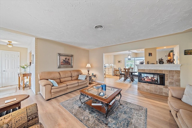 living room featuring light hardwood / wood-style flooring, a textured ceiling, and a tile fireplace