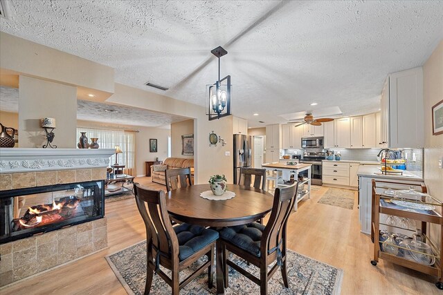 dining room with sink, a textured ceiling, a fireplace, ceiling fan with notable chandelier, and light hardwood / wood-style floors