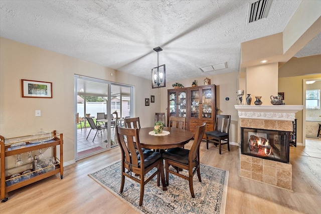 dining space with a textured ceiling, light hardwood / wood-style flooring, a tiled fireplace, and a healthy amount of sunlight