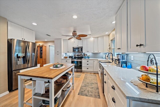 kitchen with light wood-type flooring, sink, white cabinets, stainless steel appliances, and light stone countertops