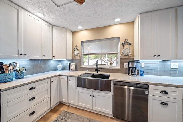 kitchen featuring sink, stainless steel dishwasher, white cabinetry, light wood-type flooring, and decorative backsplash