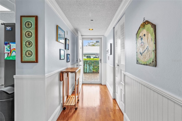 corridor featuring light wood-type flooring, a textured ceiling, and ornamental molding