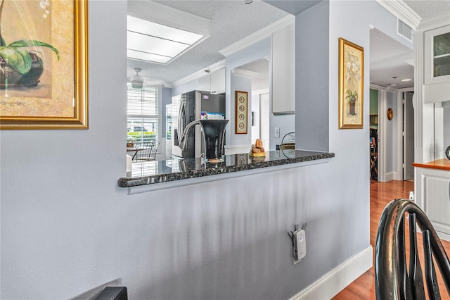 kitchen featuring light wood-type flooring, crown molding, stainless steel fridge, a textured ceiling, and ceiling fan