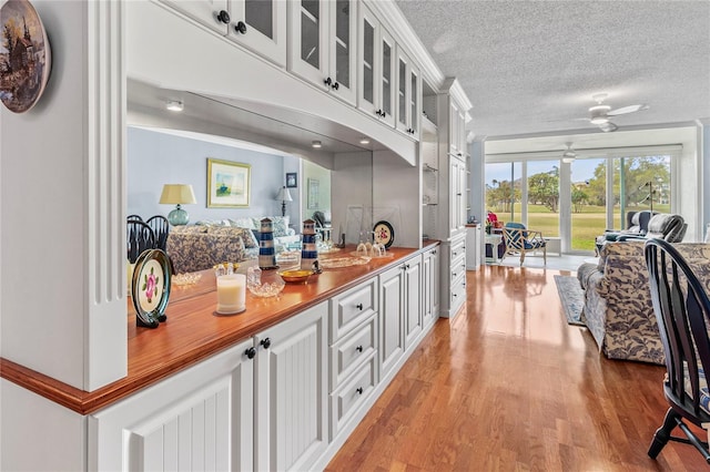 kitchen with light wood-type flooring, white cabinetry, ceiling fan, and a textured ceiling