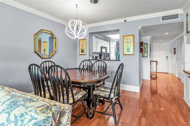 dining space featuring hardwood / wood-style flooring, an inviting chandelier, crown molding, and a textured ceiling