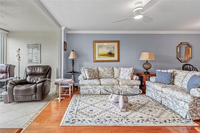 living room with light wood-type flooring, ceiling fan, a textured ceiling, and ornamental molding