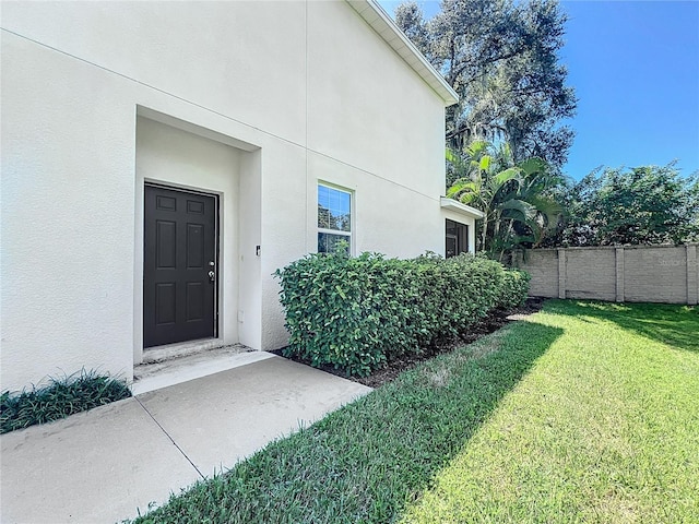property entrance featuring a lawn, fence, and stucco siding