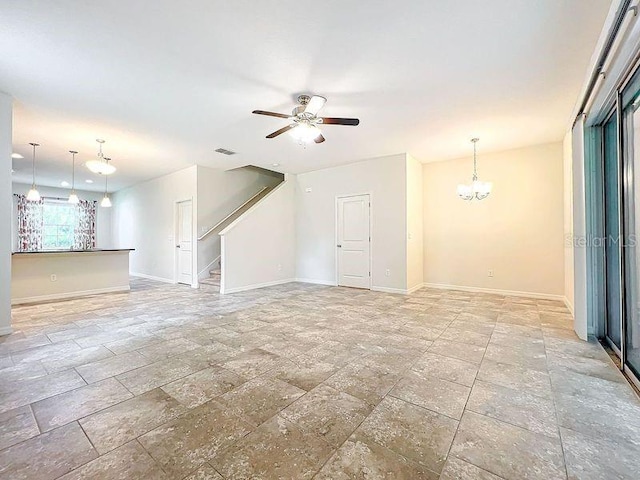 unfurnished living room featuring ceiling fan with notable chandelier, stairs, stone finish flooring, and baseboards