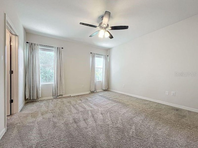 carpeted spare room featuring a ceiling fan and baseboards