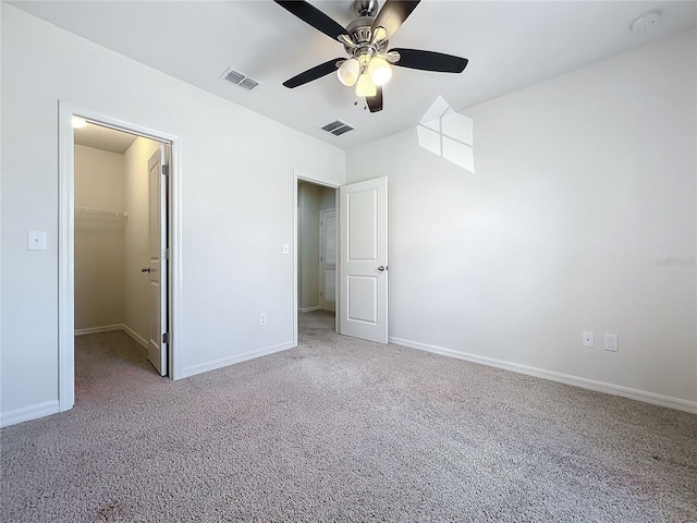 unfurnished bedroom featuring a spacious closet, a closet, ceiling fan, and light carpet