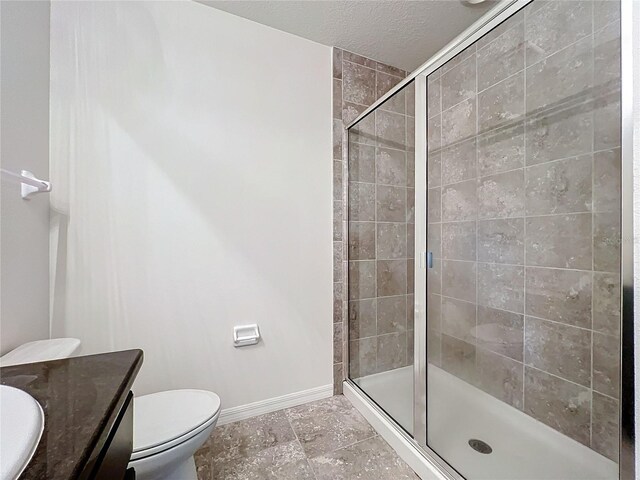 bathroom with a textured ceiling, vanity, toilet, and a shower with shower door