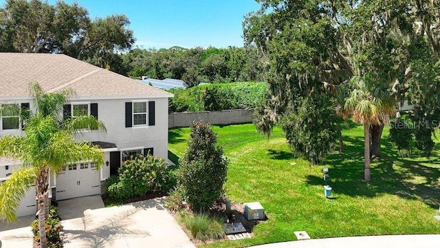 exterior space with concrete driveway, stucco siding, fence, a garage, and a lawn