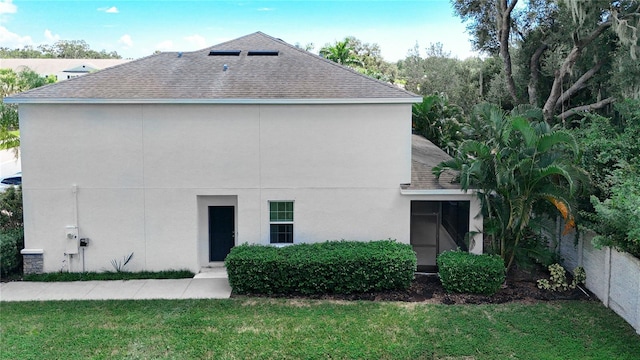 back of house featuring a lawn, a shingled roof, fence, and stucco siding