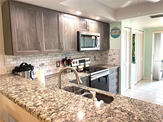 kitchen with light stone counters, a sink, backsplash, appliances with stainless steel finishes, and light tile patterned floors