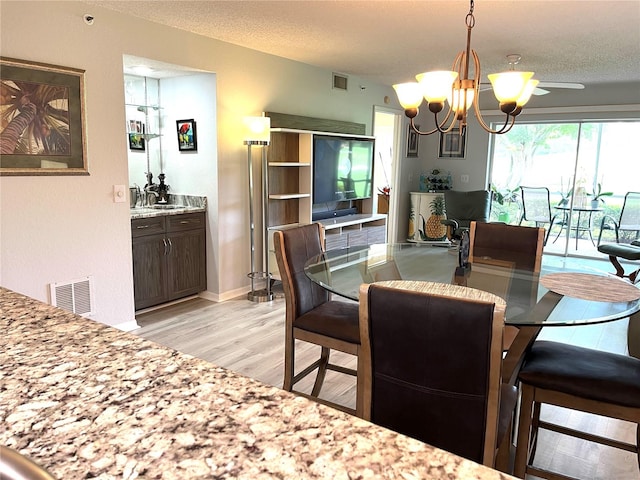 dining space with light wood finished floors, visible vents, a textured ceiling, and a chandelier