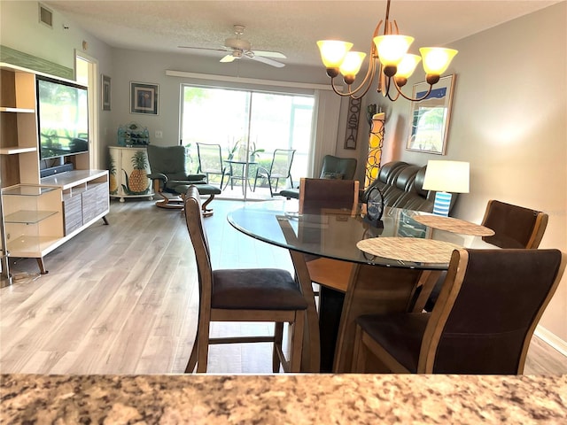 dining room with ceiling fan with notable chandelier, wood finished floors, visible vents, and a textured ceiling