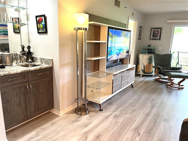 living area featuring baseboards, visible vents, a textured ceiling, and light wood-style floors