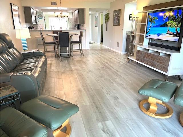 living room with visible vents, baseboards, light wood-style floors, and an inviting chandelier