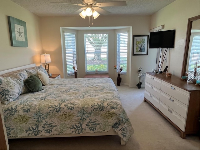 bedroom featuring light colored carpet, a ceiling fan, and a textured ceiling